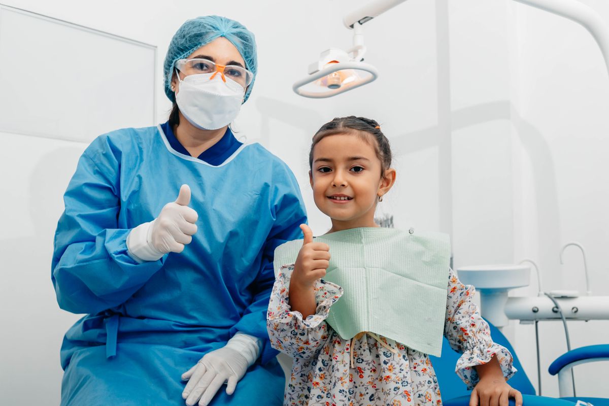 Niña sonriendo con el pulgar arriba junto a su odontóloga